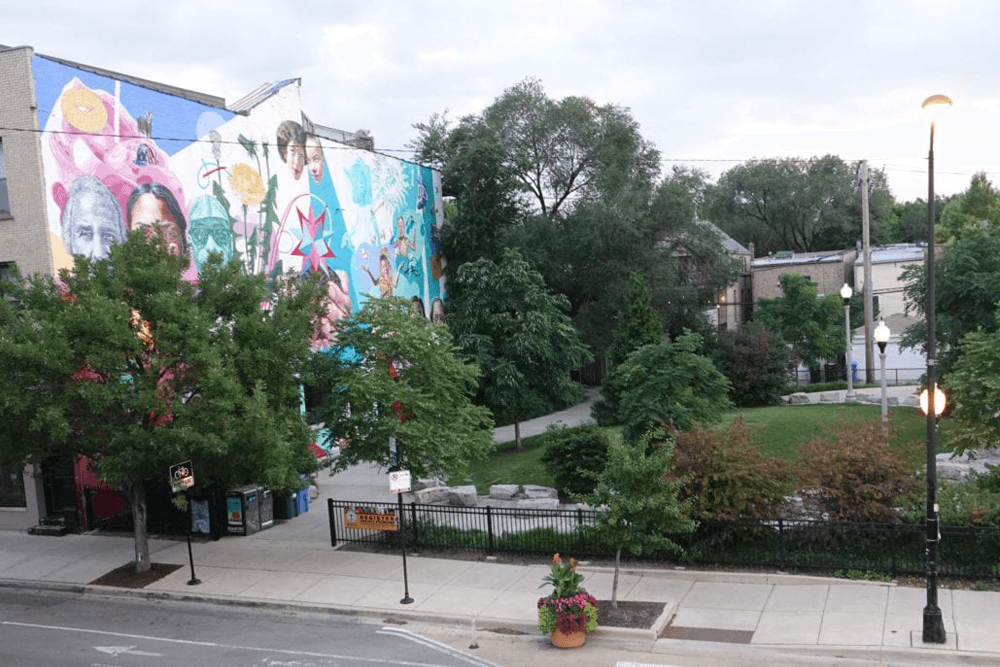 A colorful mural adorns a building beside a green park with trees and walking paths.