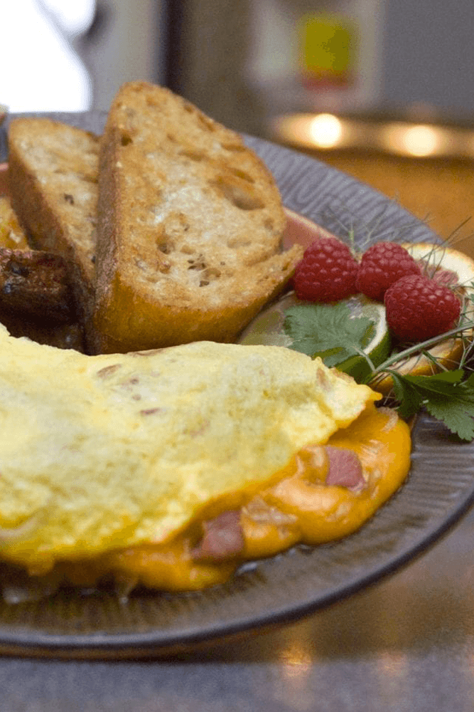 A plate featuring a cheese omelette, toast, raspberries, and garnishes.