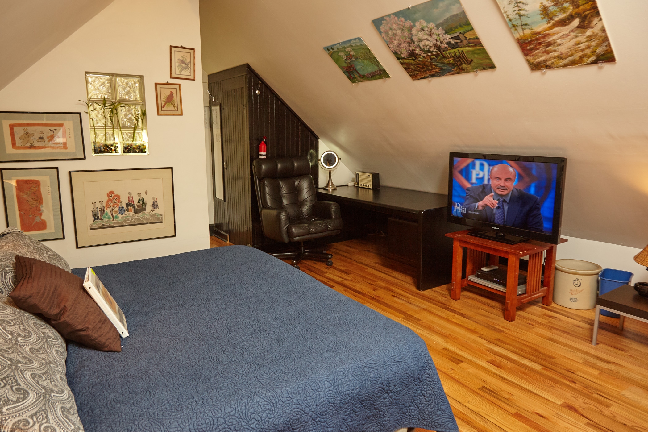 king bed with green comforter, two padded rolling chairs, oak floors, 2 double-hung and one picture  windows.