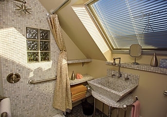 large window with black blinds, marble tiled sink and shower walls and marble tiled shelf with orange towels