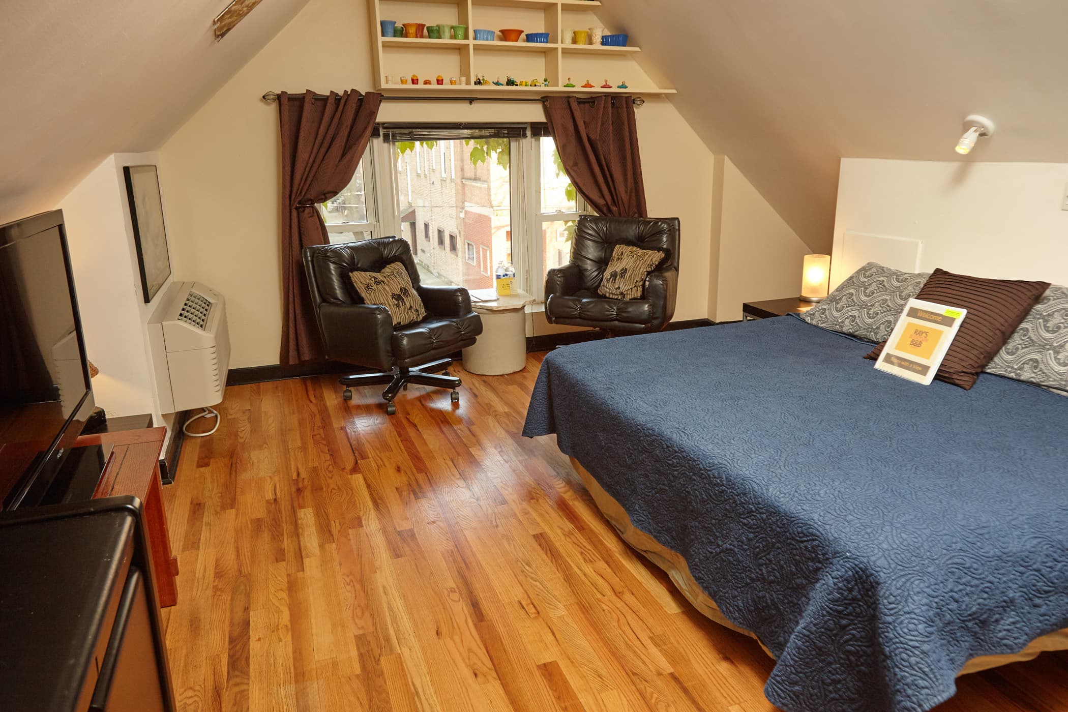 king bed with green comforter, padded rolling chair, oak floors, large black desk.