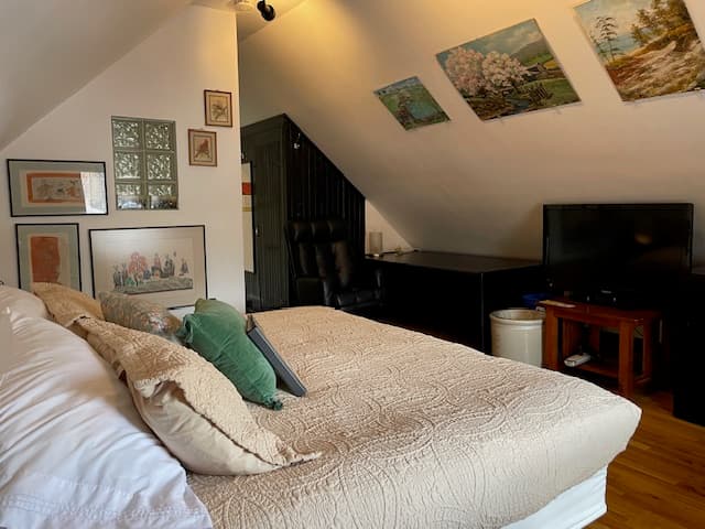 king bed with green comforter, padded rolling chair, oak floors, large black desk.