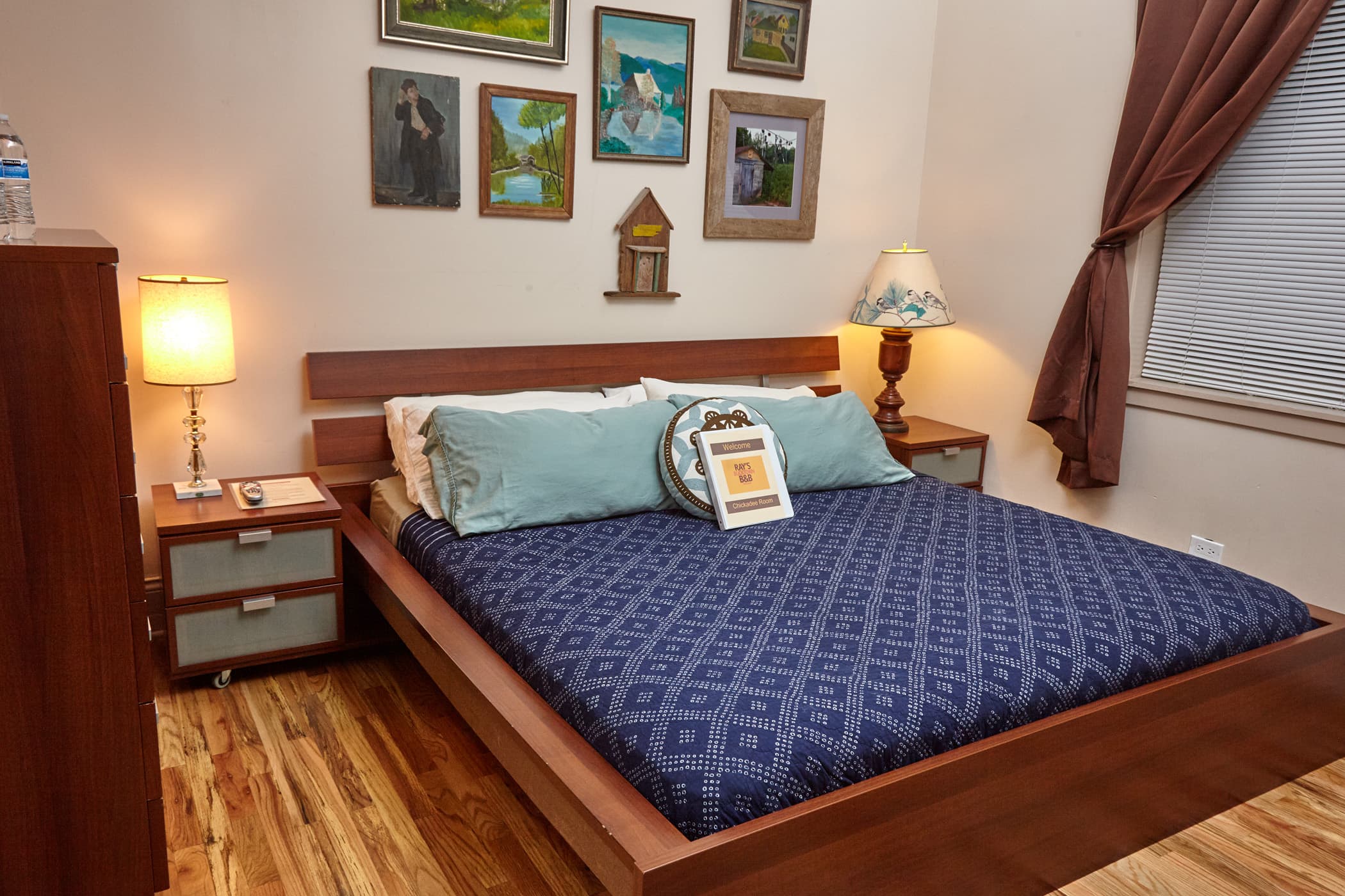 King bed with tan sheets and dark brown comforter with tan walls with old original paintings on wall.  oak wood floors