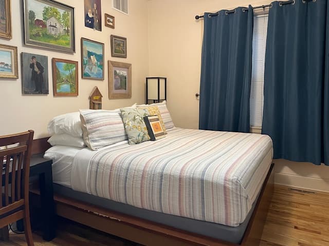 King bed with tan sheets and dark brown comforter with tan walls with old original paintings on wall.  oak wood floors