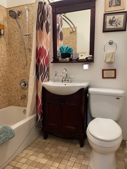 tumbled stone tile shower wall, white tub, light brown tumbled stone tile floors, white ceramic toilet & sink