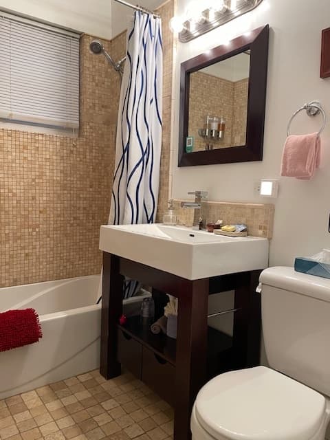 white bathtub with shower head and brown shower curtain, white sink top and waterfall faucet