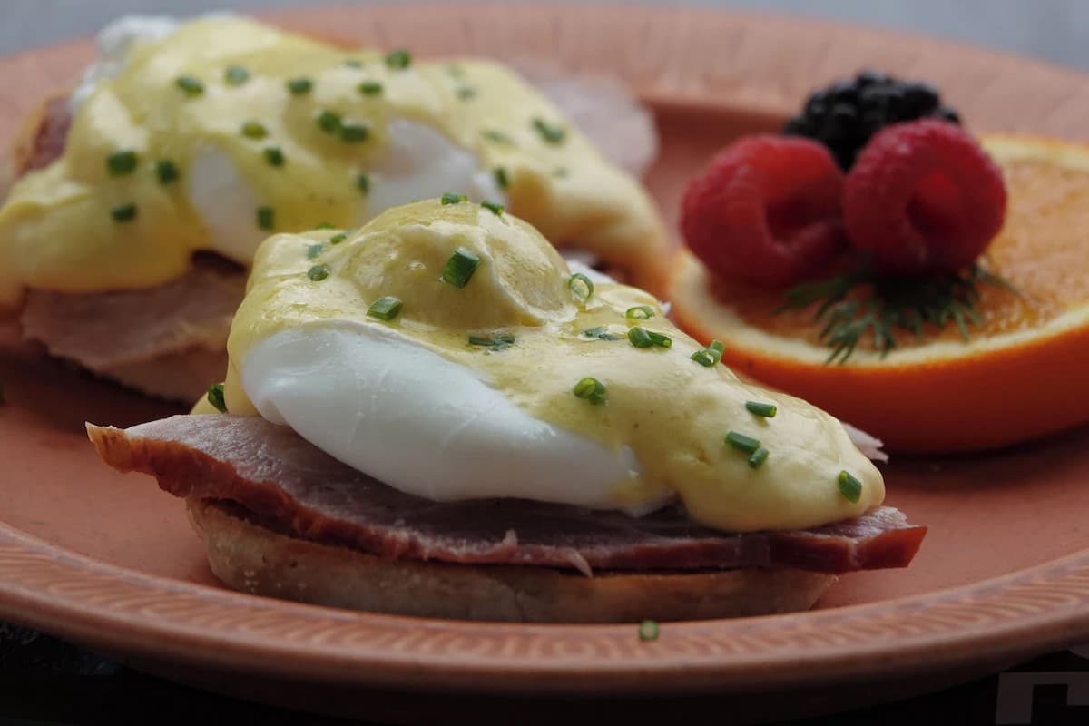 A plate of Eggs Benedict with poached eggs and hollandaise sauce, served with fresh fruit.