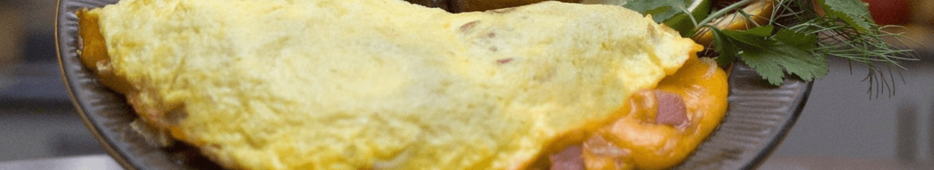 A fluffy omelette with melted cheese and ham, garnished with fresh herbs.