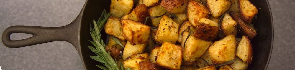 A cast-iron skillet filled with golden roasted potatoes garnished with herbs.