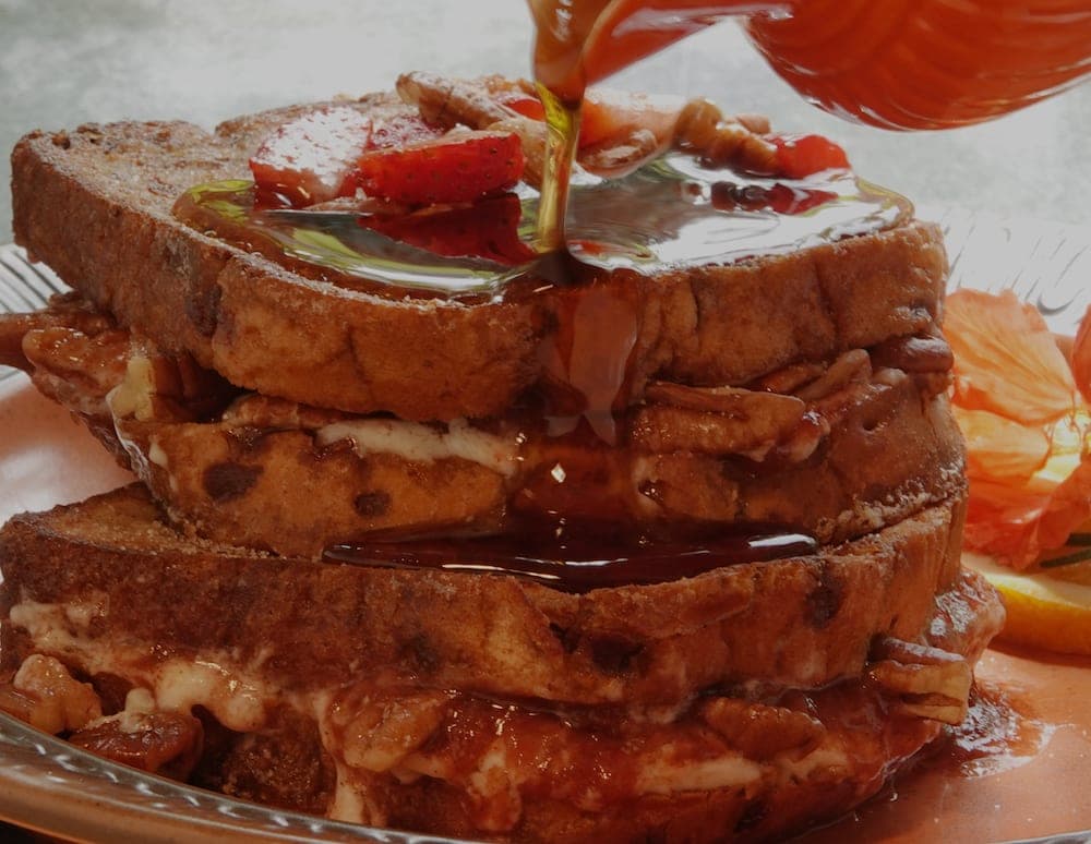 A stack of French toast topped with syrup, strawberries, and pecans.